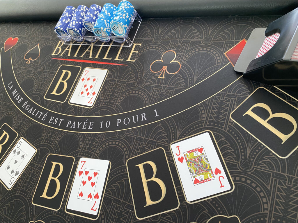 Table du jeu La Bataille avec cartes retournées et jetons bleus sur tapis noir et or La Bataille - jeu de cartes casino simple