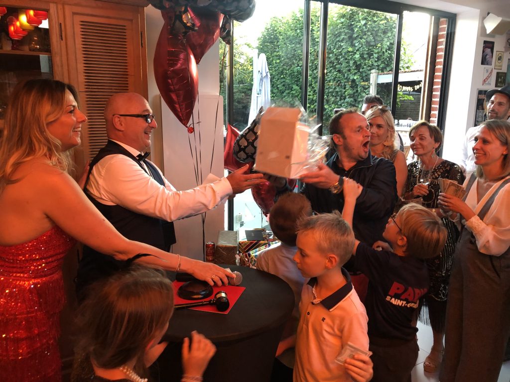 Vente aux Enchères Festive Animateur en gilet remettant un lot emballé à un gagnant enthousiaste avec marteau de commissaire-priseur sur la table